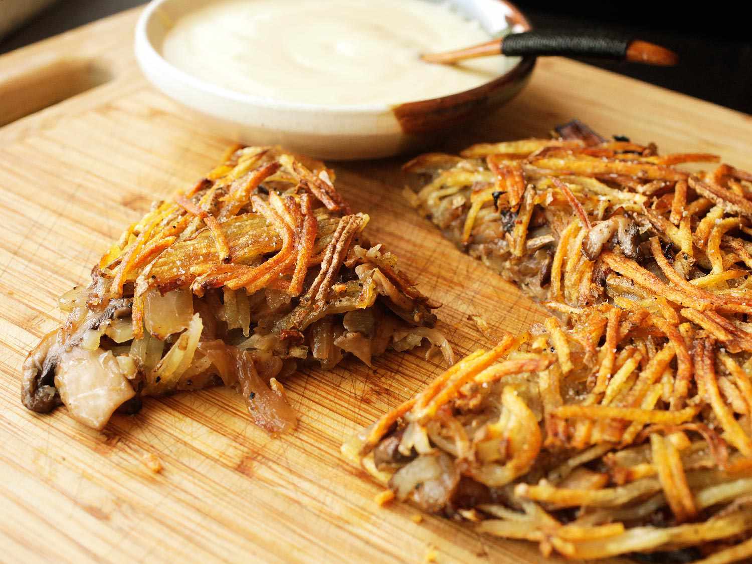 Potato and mushroom rosti with a bowl of sour cream in the background.