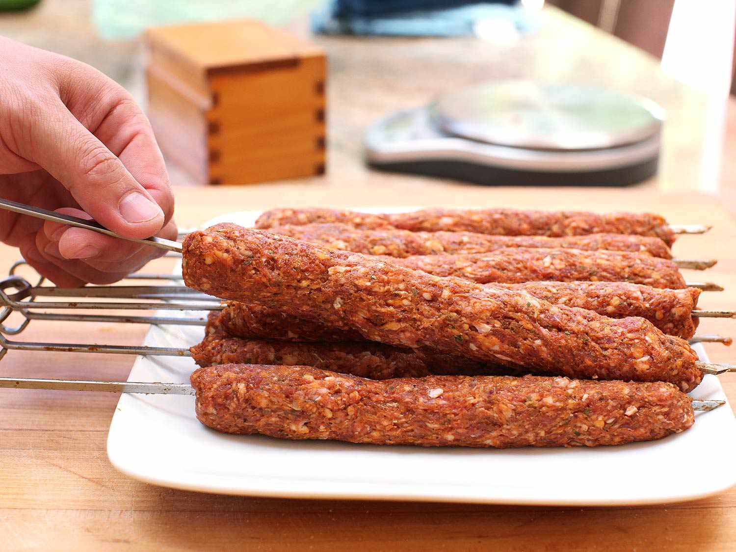Author taking a skewer of seekh kebab out of a white plate containing a few more skewers. 