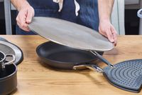 a person placing the bergkoch splatter screen over a skillet