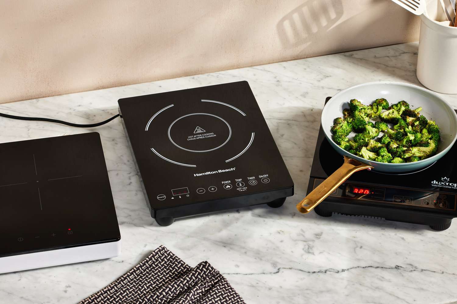 Three portable induction cooktops sit on a marble countertop. 
