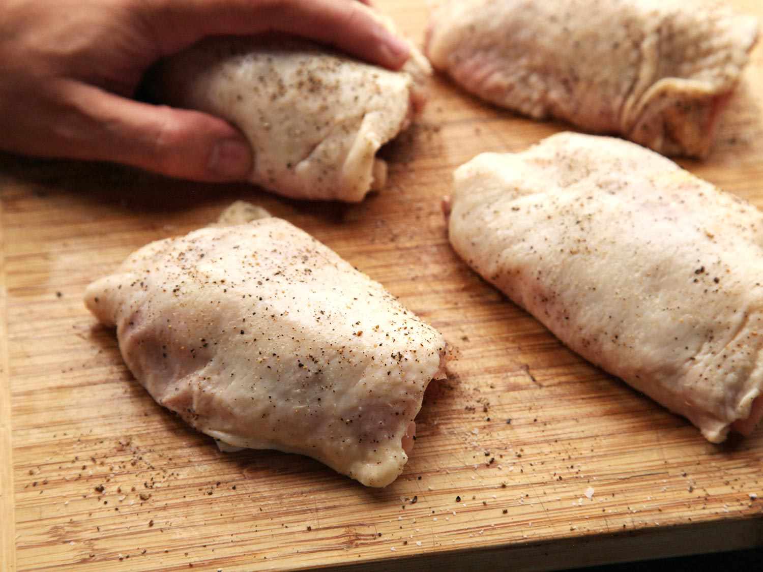 Chicken thighs are seasoned on a cutting board.