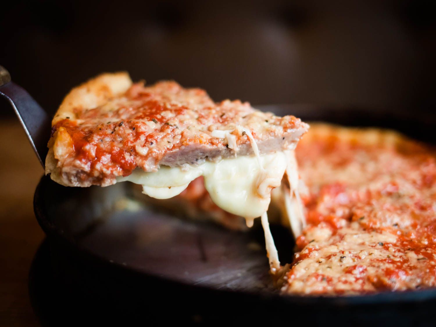 A slice of deep dish pizza from Lou Malnati's is held up to the camera with a spatula.