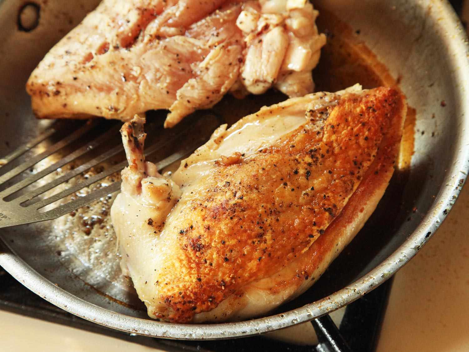 Two pieces of chicken cooking and being flipped in a skillet.