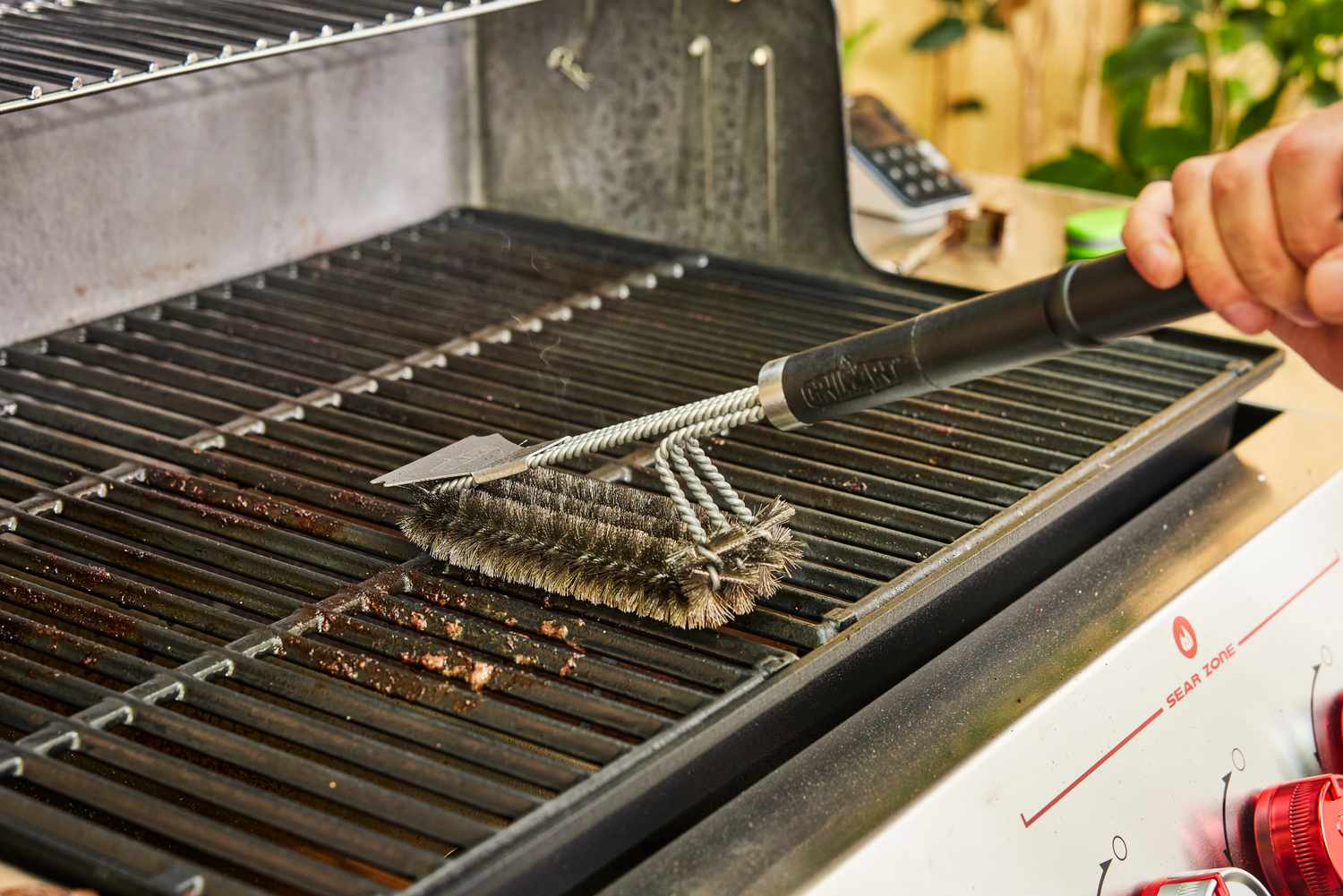 A person uses a grill brush to clean the Weber Genesis E-325 Liquid Propane Gas Grill