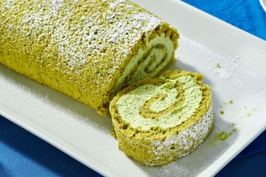 Matcha Swiss roll on a white plate sliced to show the spiraled filling