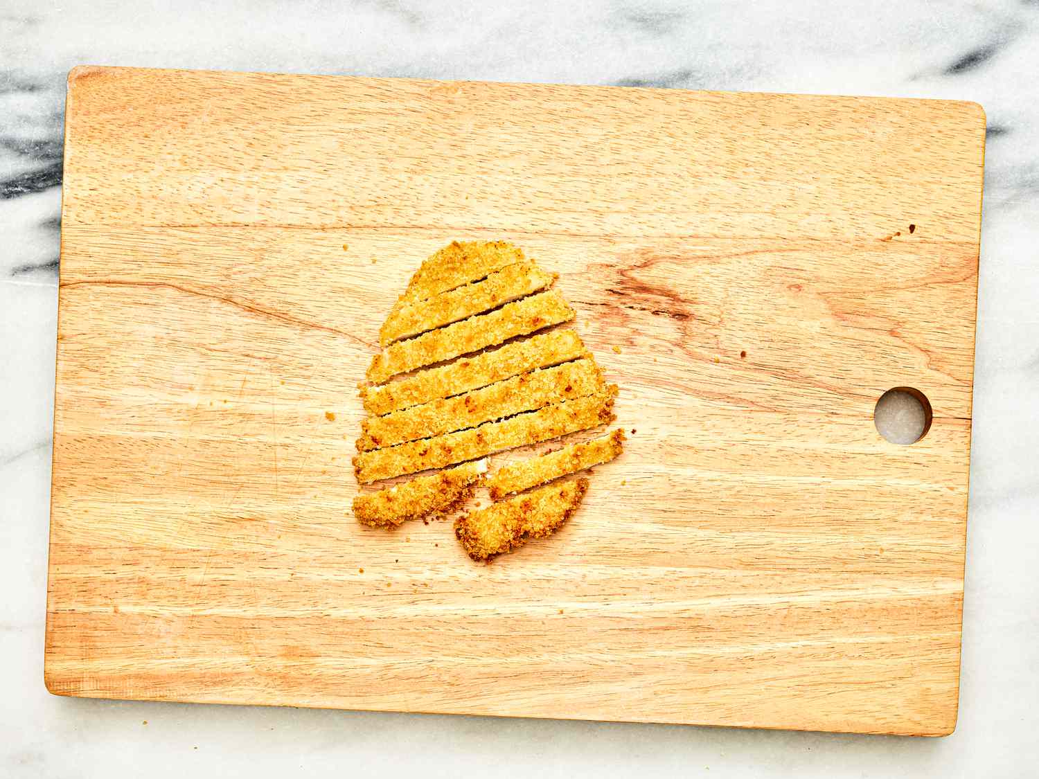 The finished air fryer chicken katsu cutlet, cut into strips on a wooden cutting board.