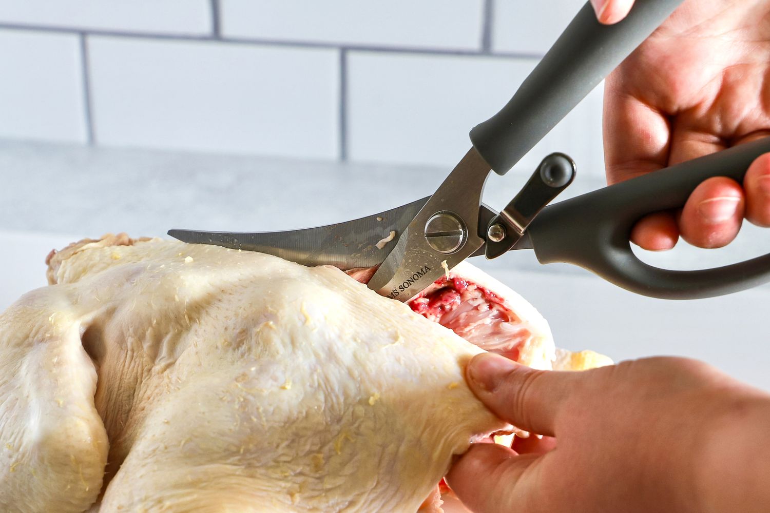 A person cutting a raw chicken with Williams Sonoma poultry shears