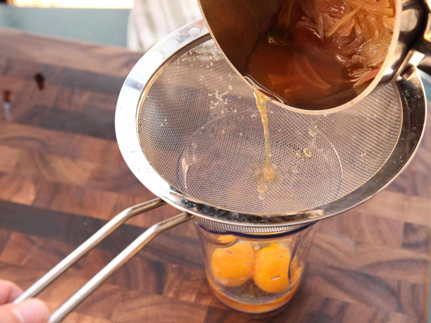 Pouring infused vinegar through strainer into jar with egg yolks to make easy bearnaise sauce