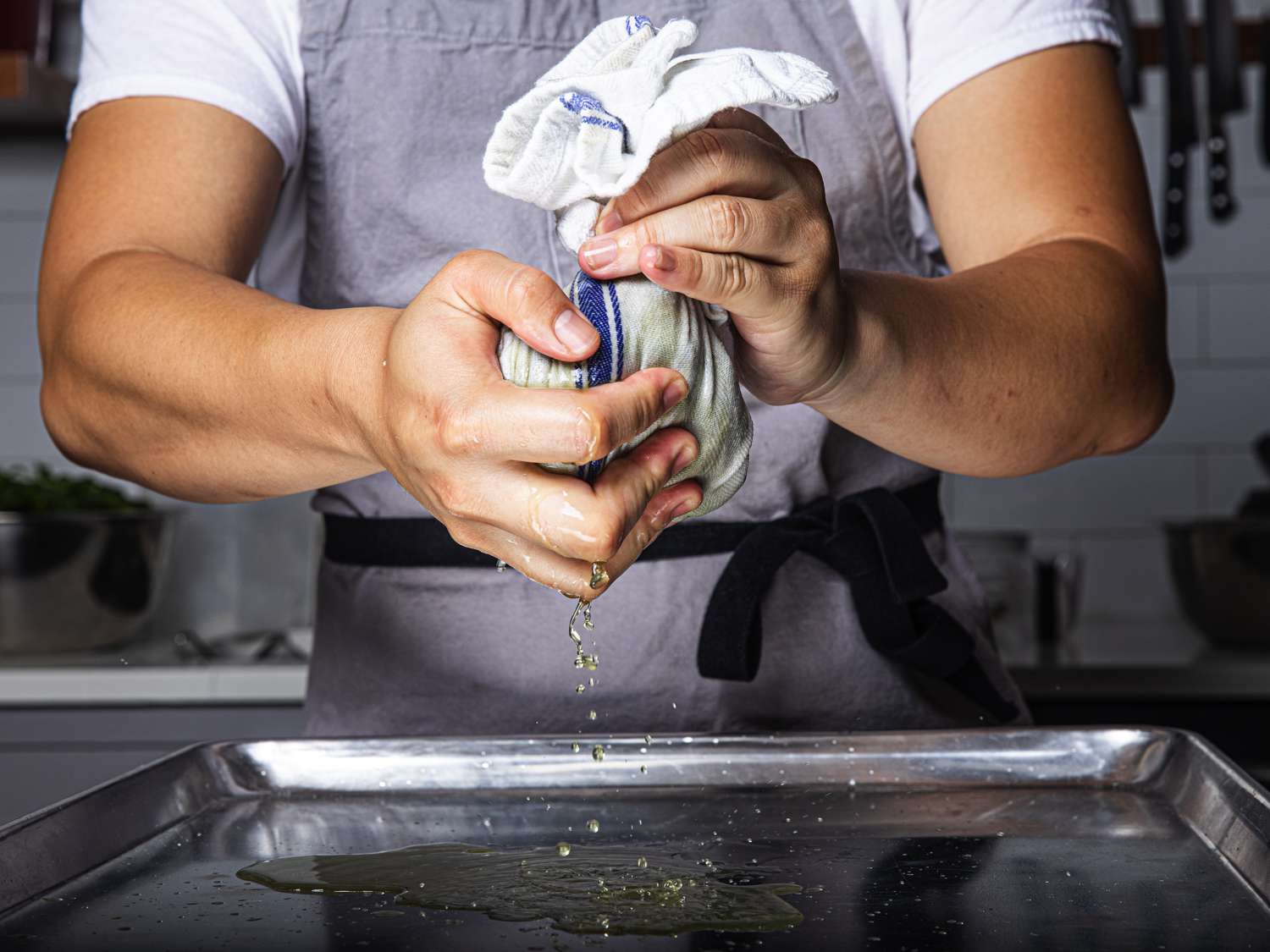 Hands wringing water out of spinach wrapped in a towel