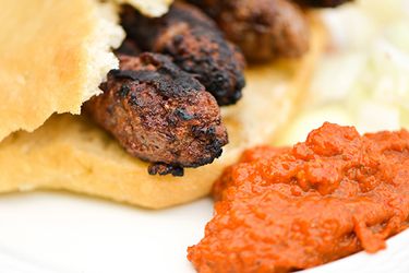 Close-up of cevapi tucked inside Serbian bread with roasted red pepper and eggplant sauce on the side