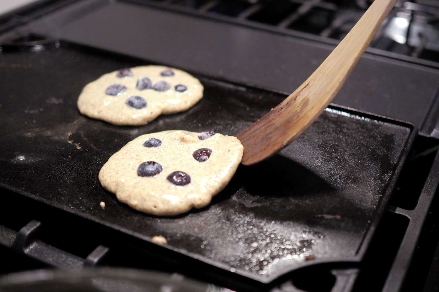 Lodge Reversible griddle with blueberry pancakes and a wooden spoon turning one over