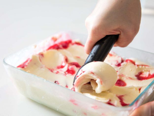 Homemade raspberry ripple goat's milk gelato being scooped out of a glass container.