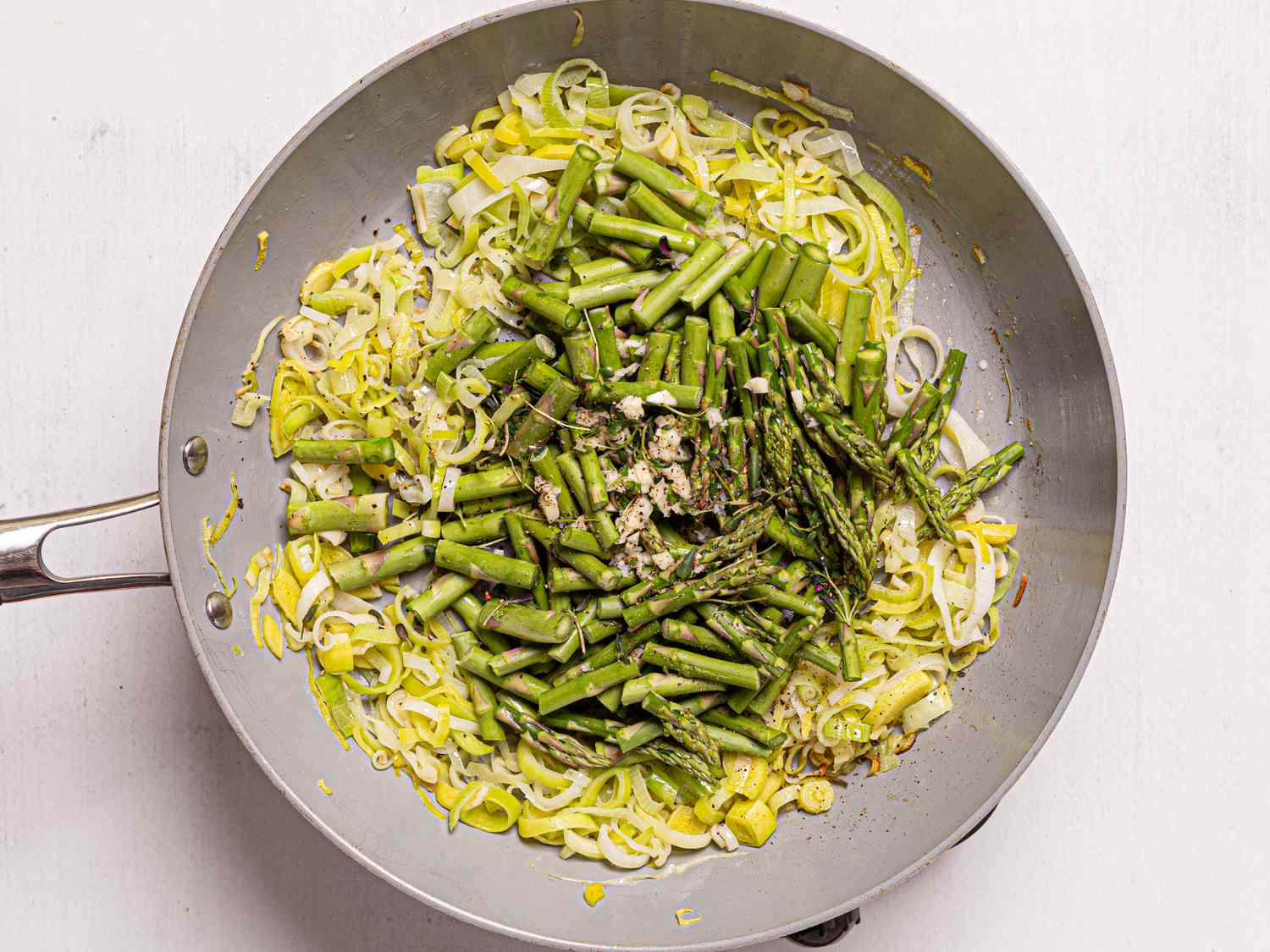 Sautéed asparagus and leeks in a pan.