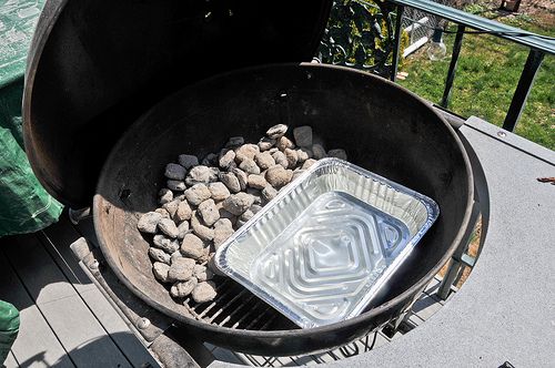 Charcoal set up on one side of kettle grill beside aluminum pan filled with water