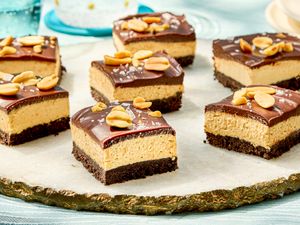 Chocolate peanut butter cheesecake bars garnished with peanuts arranged on a serving plate