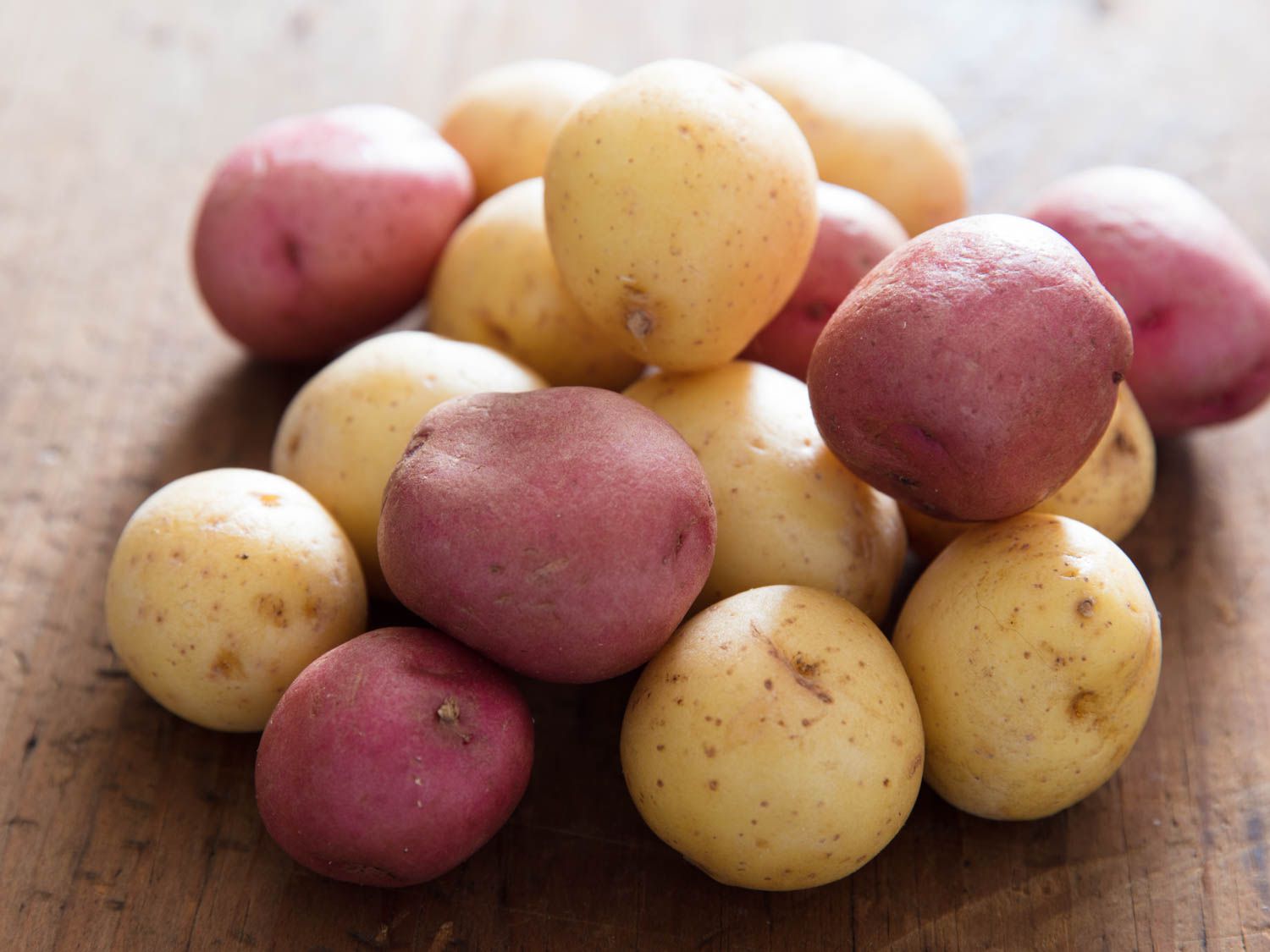A small pile of red and white new potatoes on a wooden cutting board.