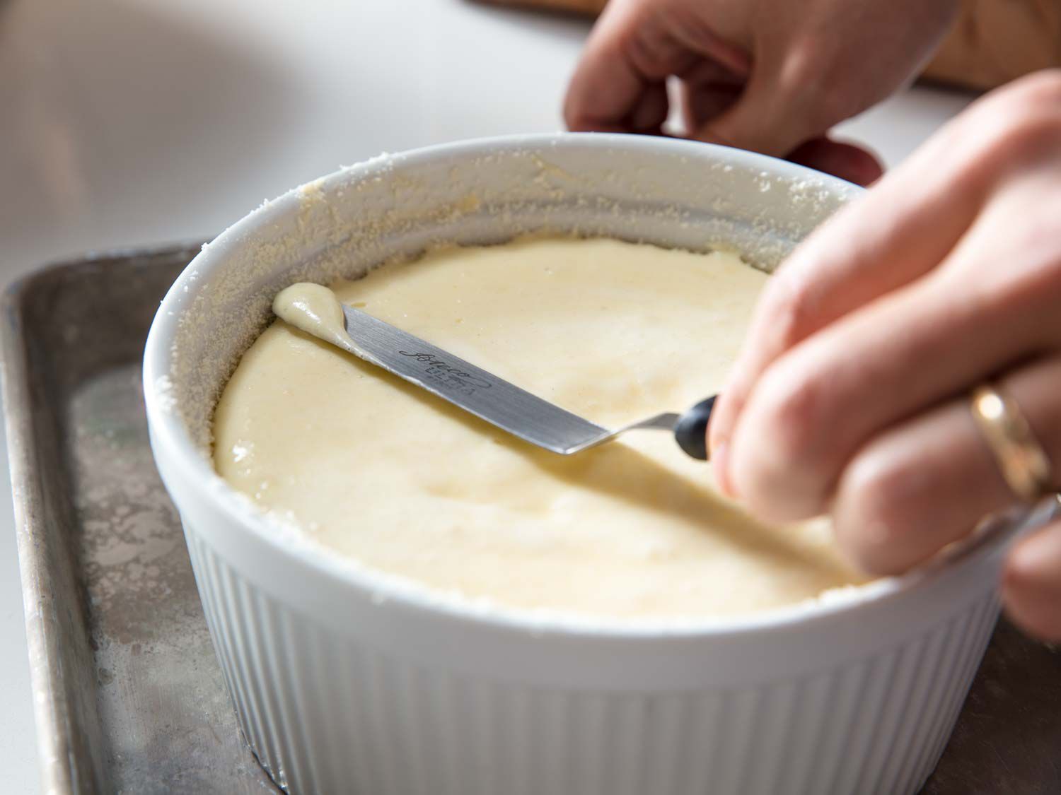 A hand using an offset spatula to smooth the top of the soufflé batter.