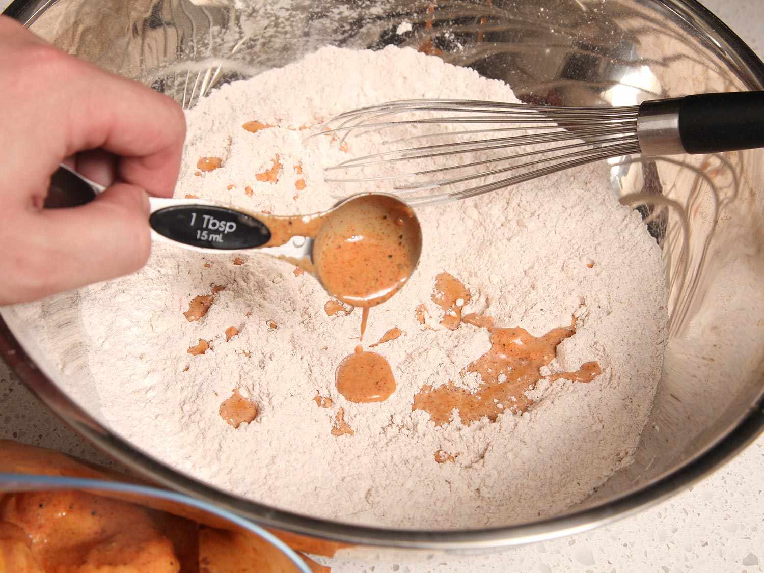Hand adding a spoonful of brine to bowl of flour mixture