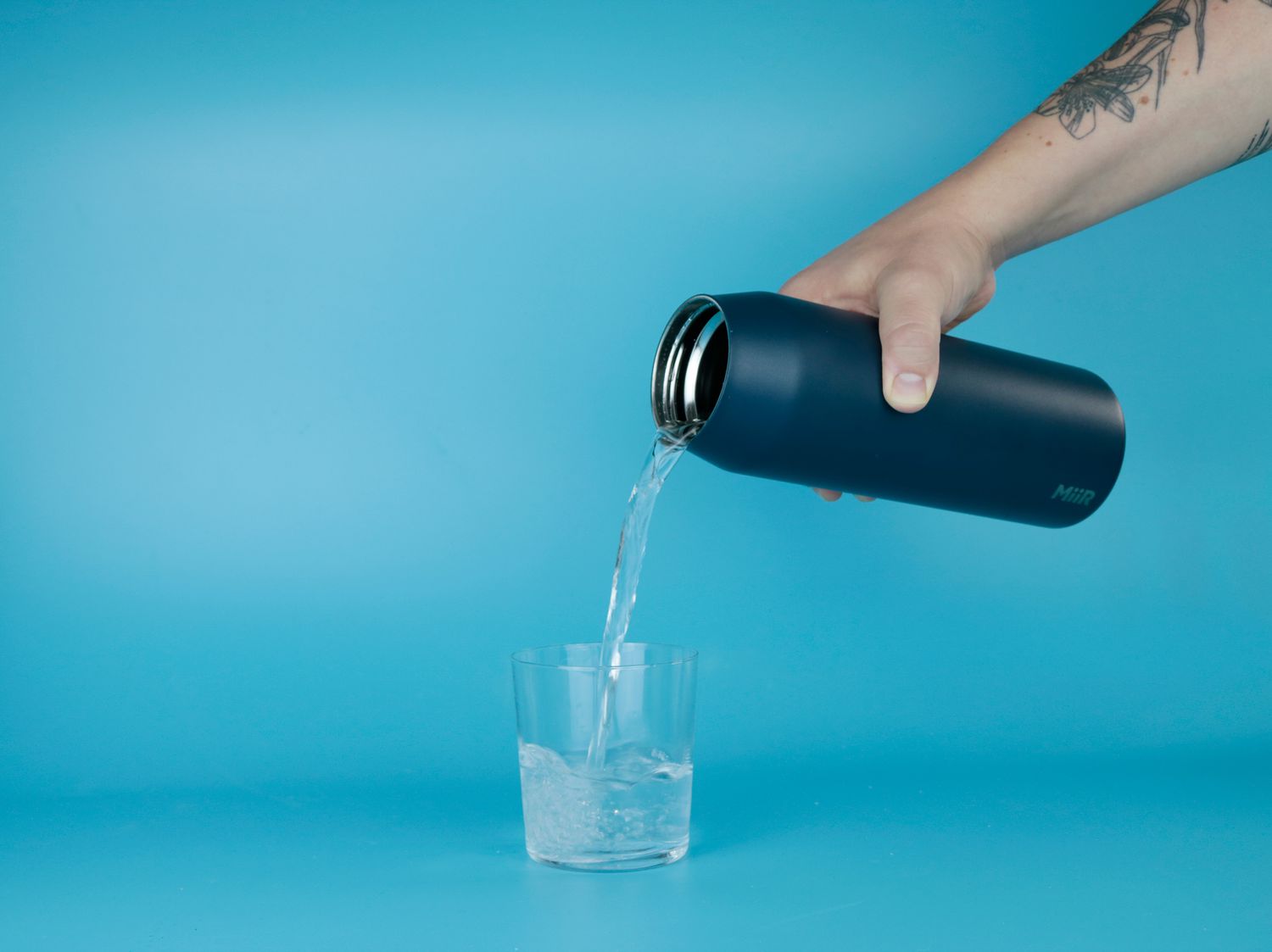 A person pouring water from a thermos into a glass