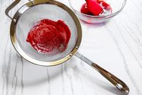 All-Clad Stainless-Steel Strainer, Set of 3 with red puree alongside a bowl with similar contents and a spatula on a surface