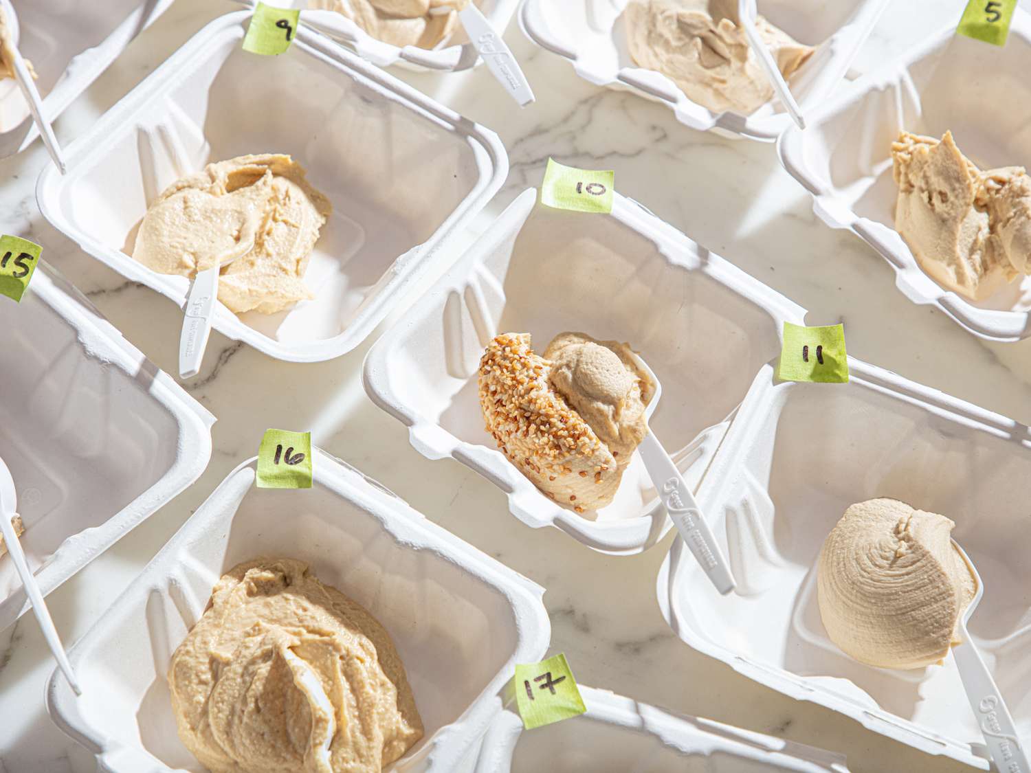 Multiple small containers holding different samples of hummus, each labeled with a number