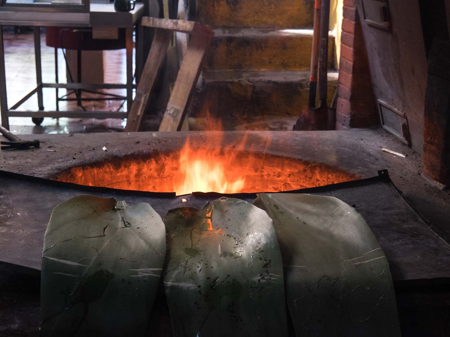 Maguey leaves lined up outside the hoyo (pit oven) in the center of Barbacoa Renatos, with a fire blazing in the oven.