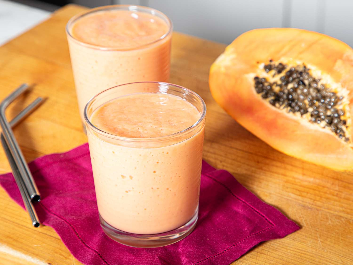 Two glasses of fruit smoothie next to half a papaya on a table
