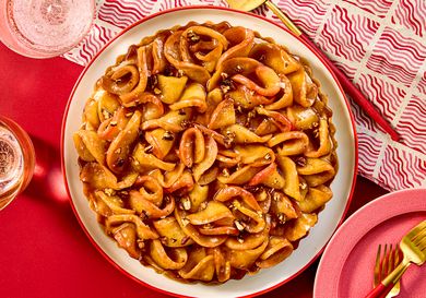 A caramel apple tart with decorative crust garnished with nuts placed on a red table setting