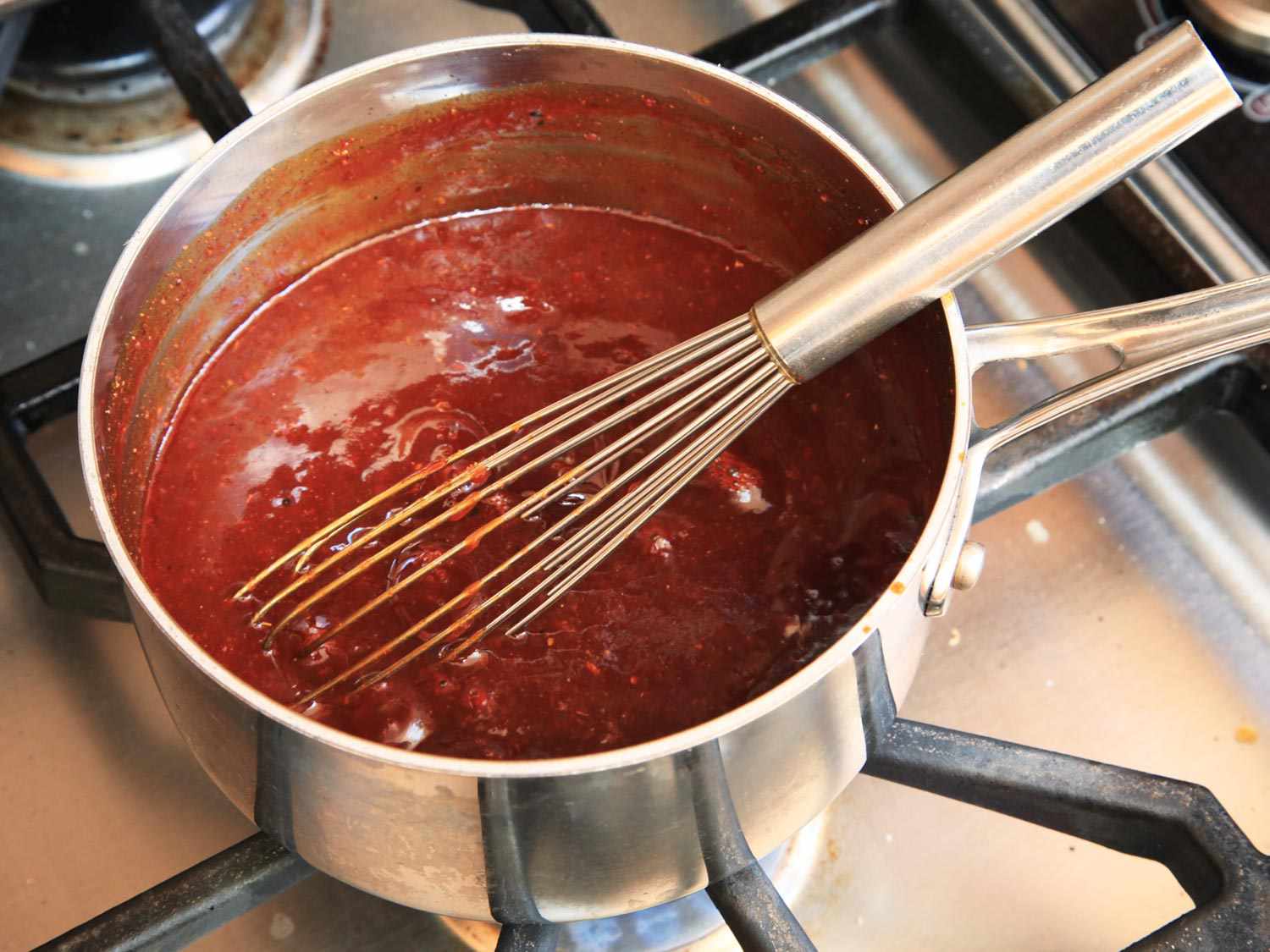 A whisk stirring a simmering Kansas-City style barbecue sauce for sous vide pork ribs.