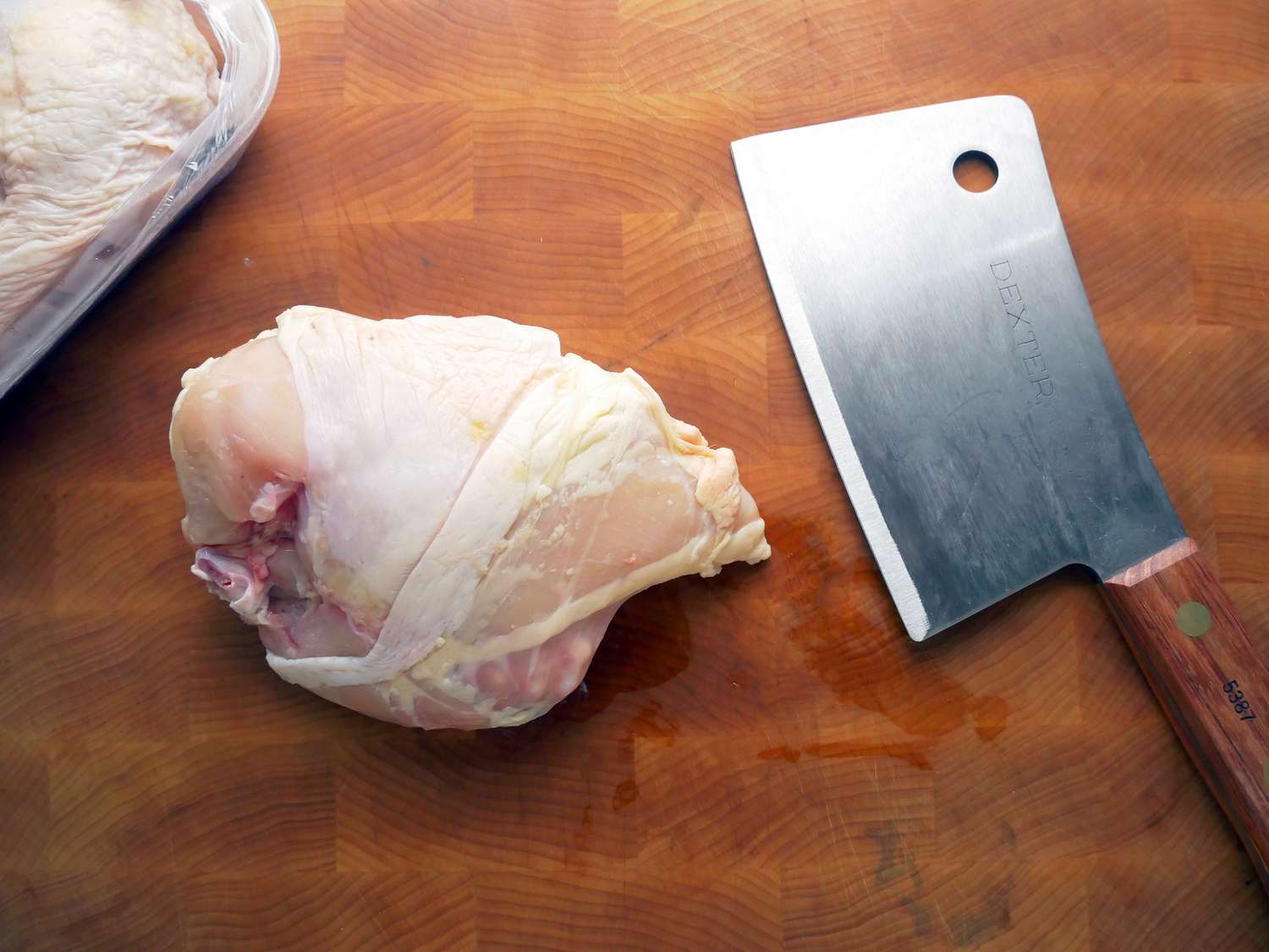 Dexter-Russell Traditional Series Cleaver on a cutting board next to uncut chicken breasts