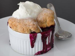 A ramekin filled with blueberry cobbler which is topped with whipped cream.