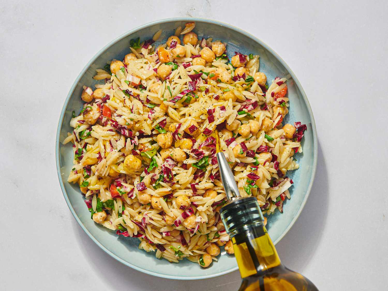 Orzo pasta salad served in a bowl with a bottle of olive oil