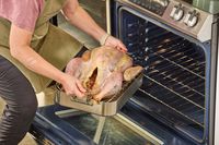 A person putting a Grassland Beef Pasture Raised Turkey into an oven