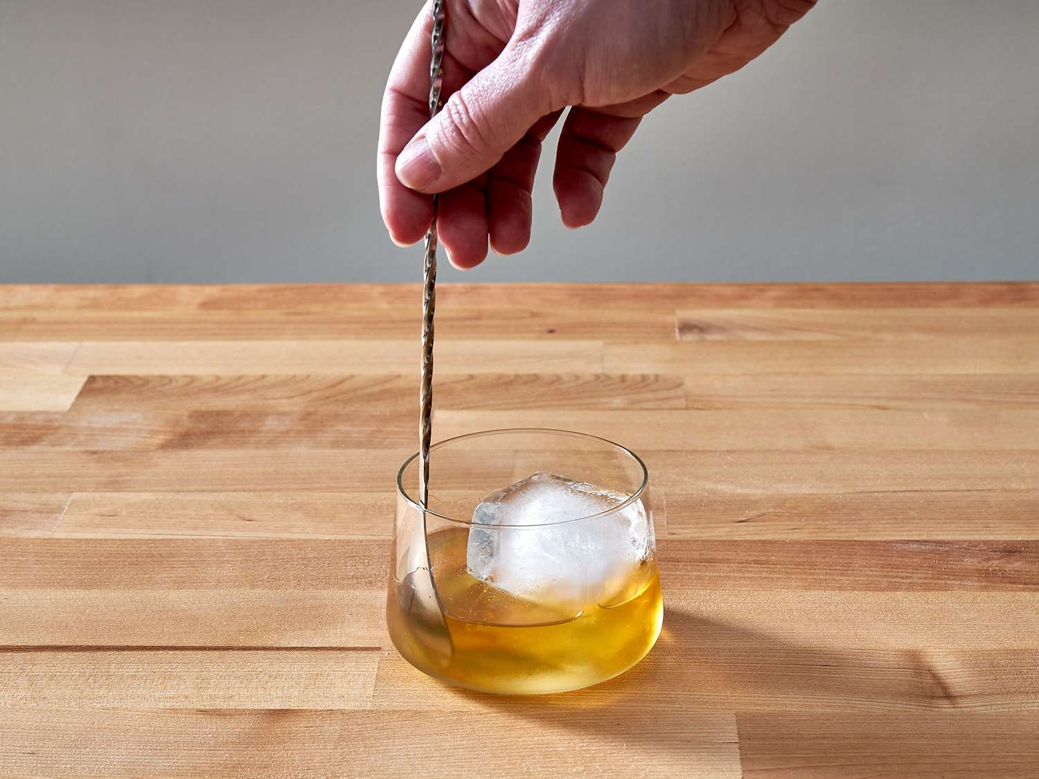 Mixing a rusty nail cocktail with a barspoon on a wooden counter.