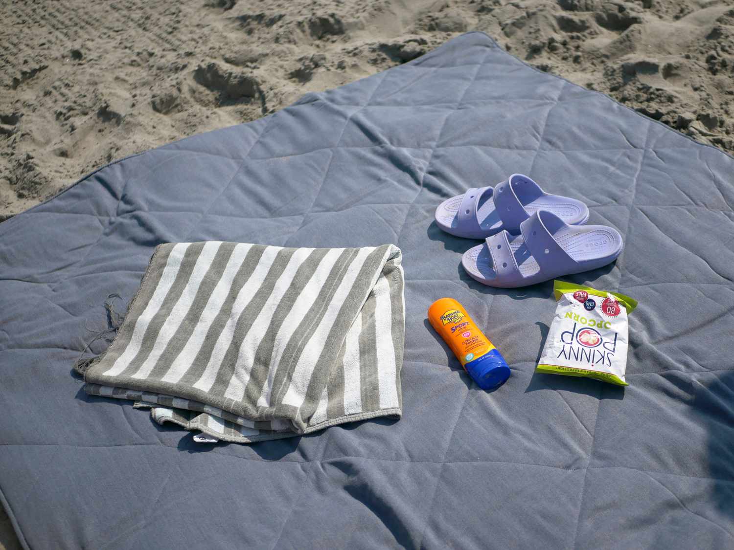 the yeti picnic blanket unfolded on the beach with a towel, sandals, sunscreen, and bag of popcorn on it