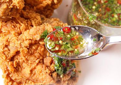 A spoonful of chile-lime-cilantro sauce being drizzled over a piece of fried chicken on a plate. 
