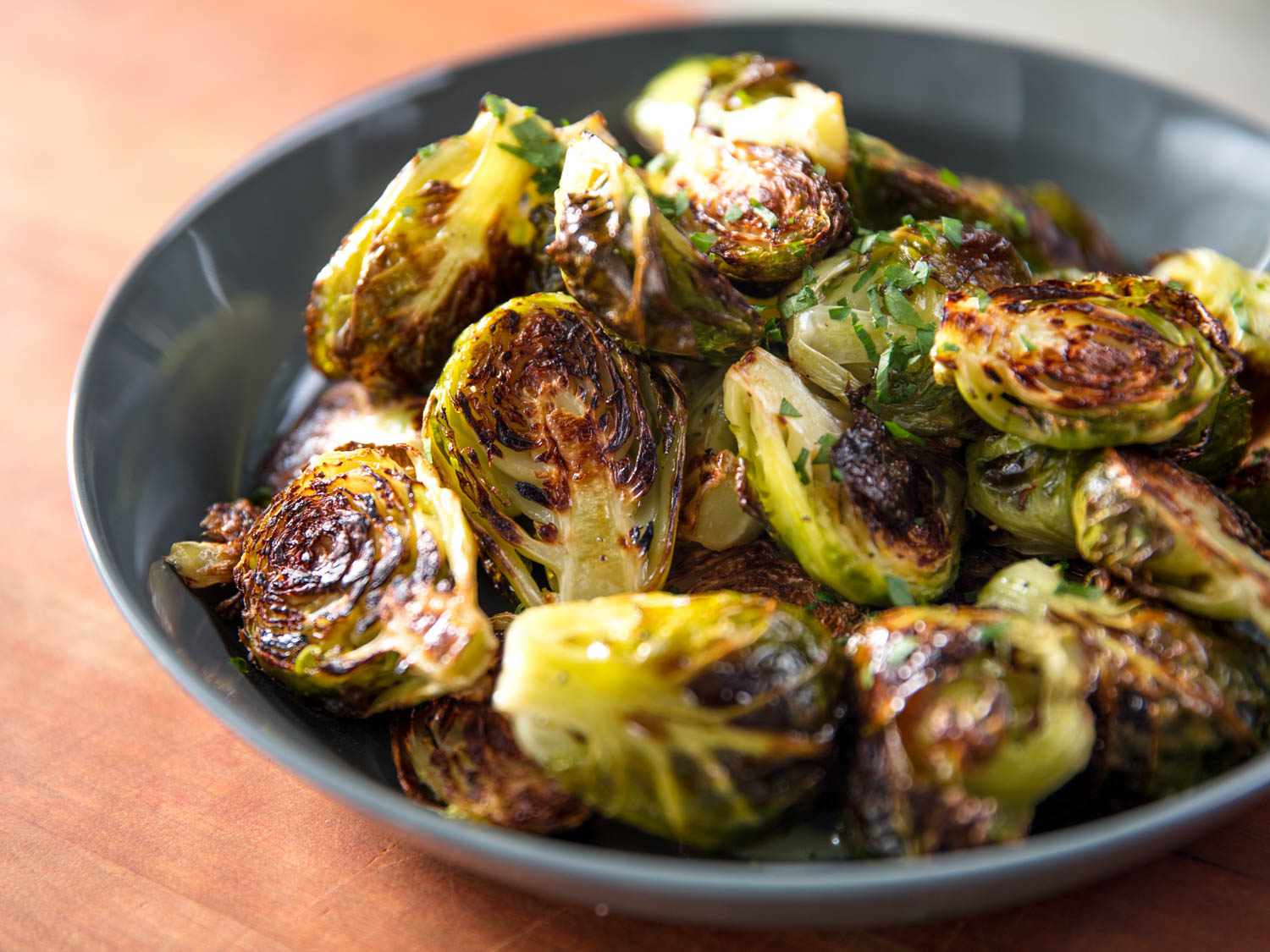 A small dark bowl of halved, roasted golden-brown Brussels sprouts.