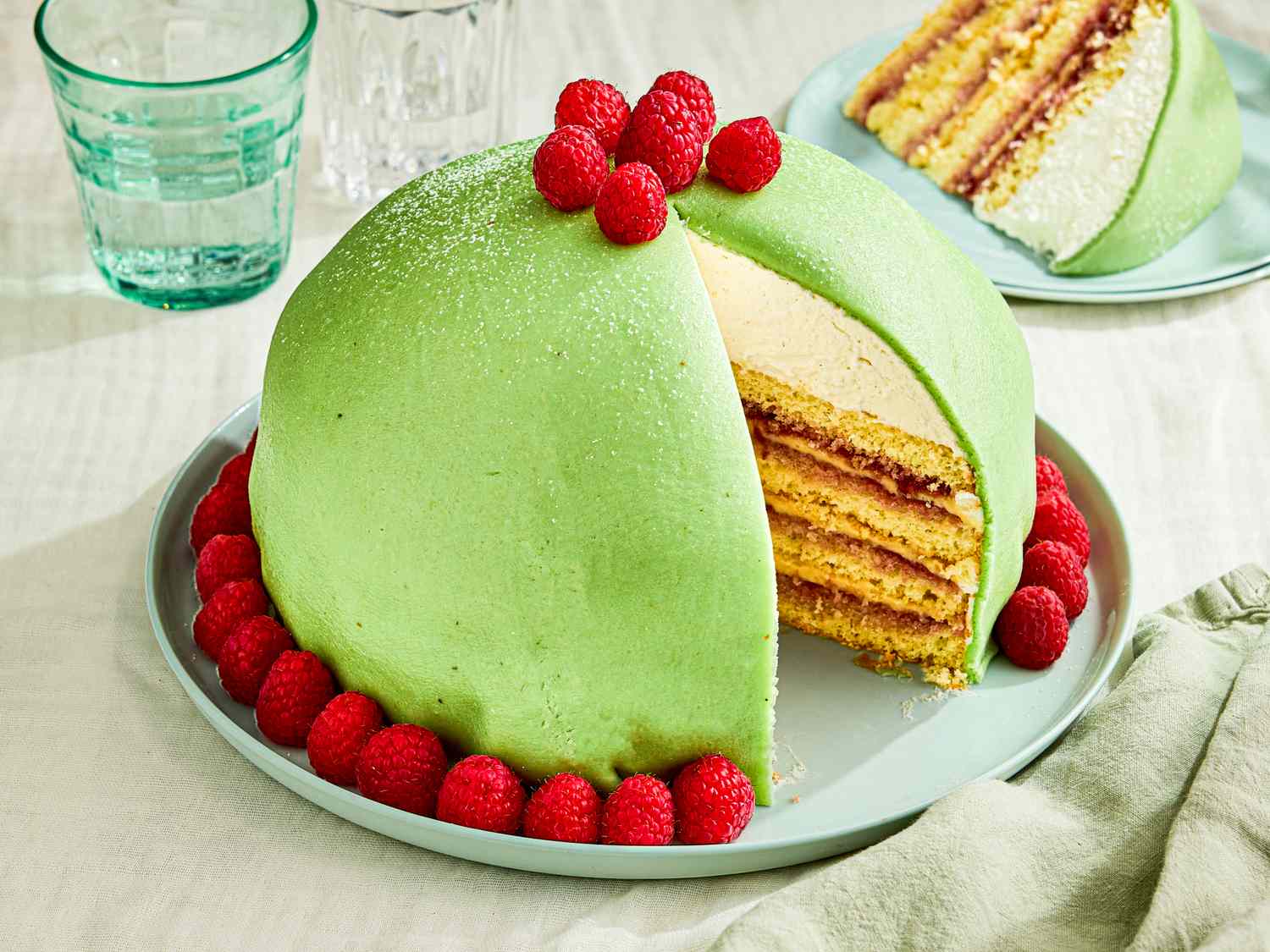 A sliced Princess cake garnished with raspberries on a plate showing its layered interior filling and marzipan cover