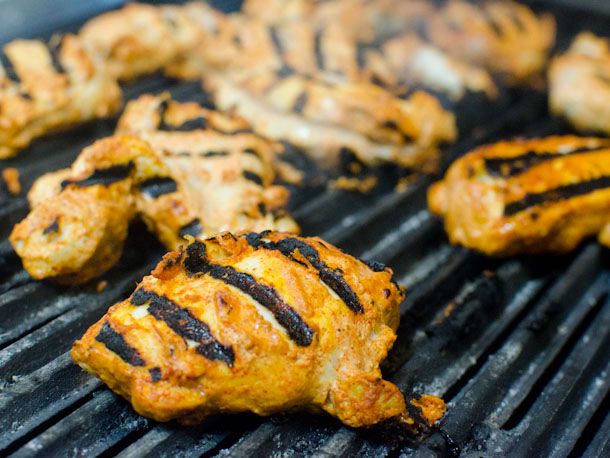 Marinated chicken thighs grilling for chicken tikka makhani. The chicken has charred marks all over.