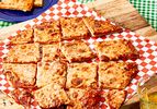A St Louisstyle pizza sliced into squares on a checkered paperlined wooden board