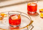 Two Negroni cocktails served in old-fashioned glasses with orange peels, with one served on a glass tray