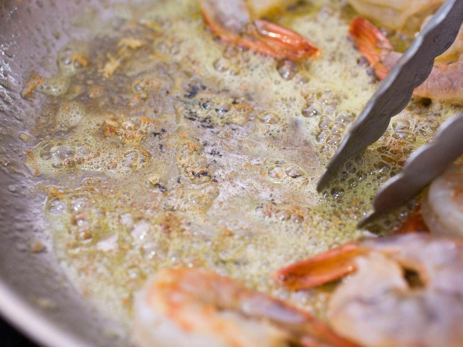 Tongs stirring shrimp sautéing in butter.
