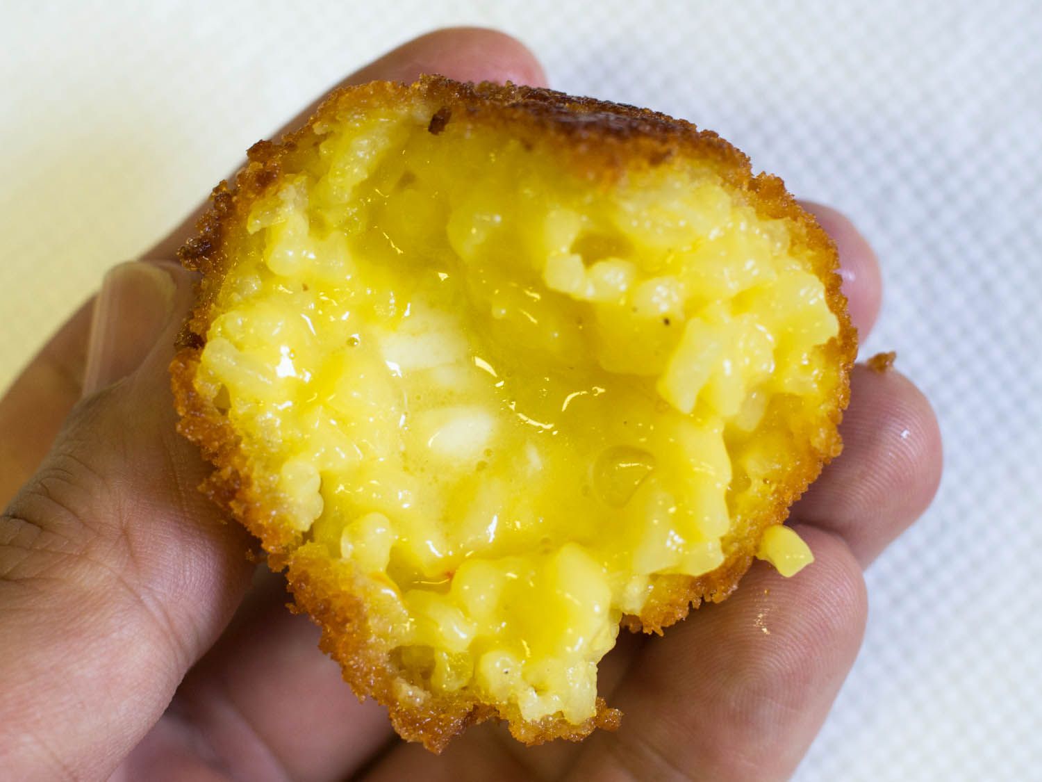 Author holding a half-eaten arancino up close to the camera lens. The interior is very moist and gooey-looking.