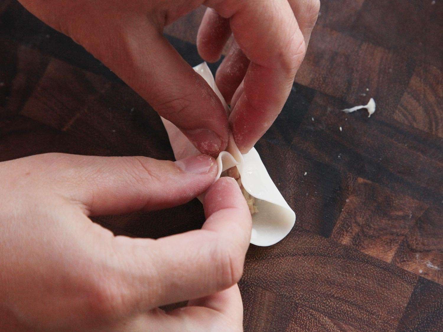 Folding pleats in a dumpling wrapper folded in half around a ground pork filling. 