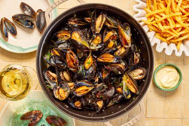 Mussles in a grey Staub Dutch oven and a side of fries.