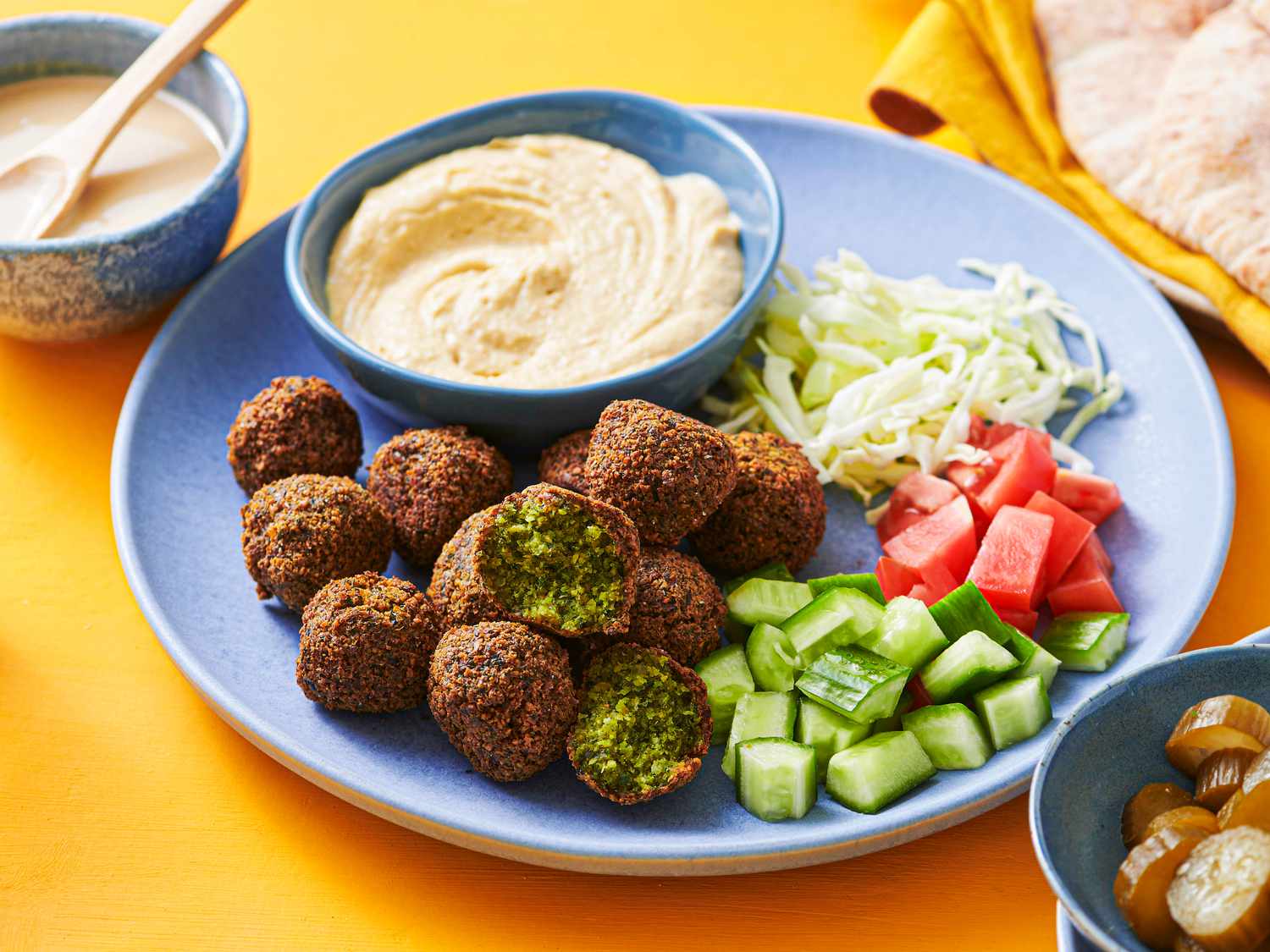 Falafels served on a plate with hummus, tomatoes, cucumber, and shredded cabbage.