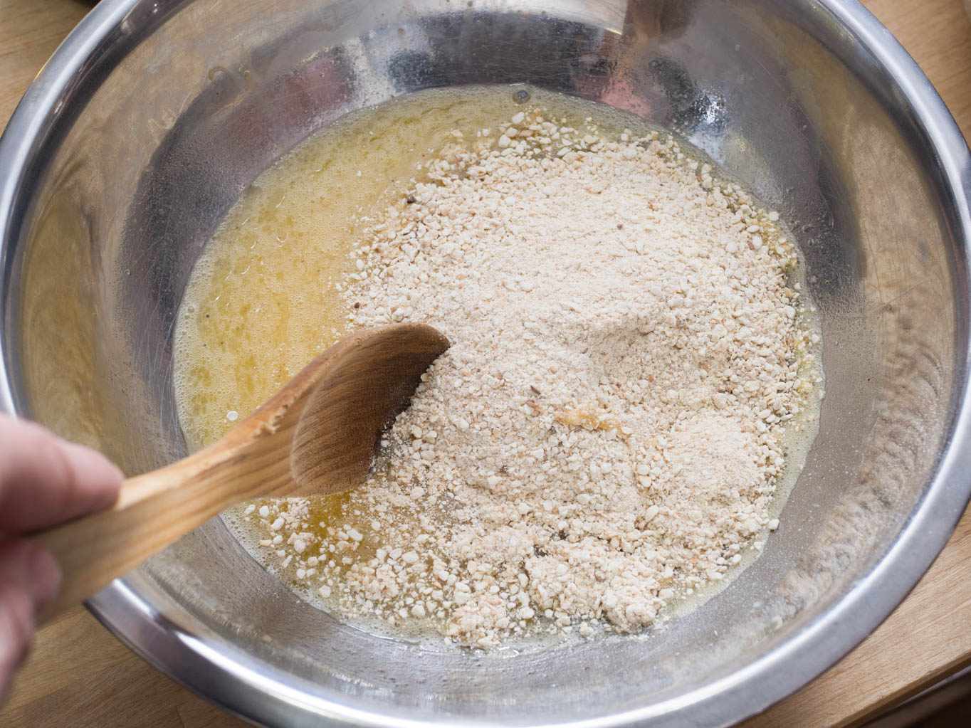 Matzo meal and the rest of the dry ingredients have been added to the egg-seltzer-schmaltz mixture and are about to get stirred together with a wooden spoon.
