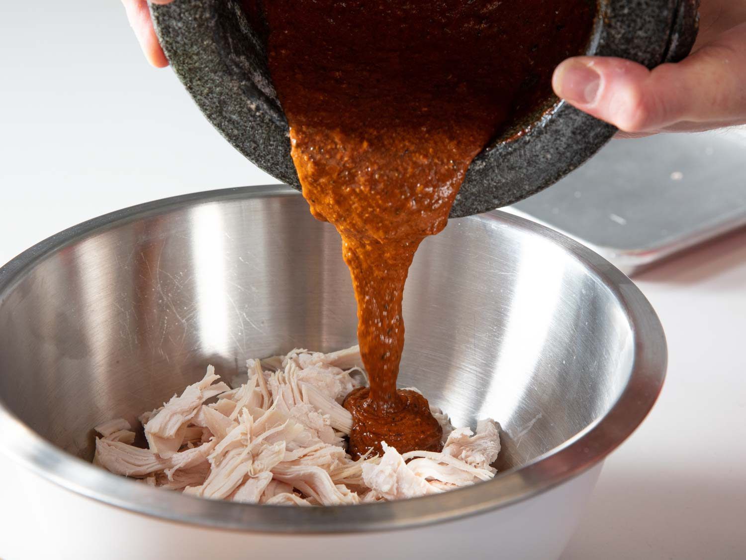 Pouring dressing into a bowl with pulled turkey.