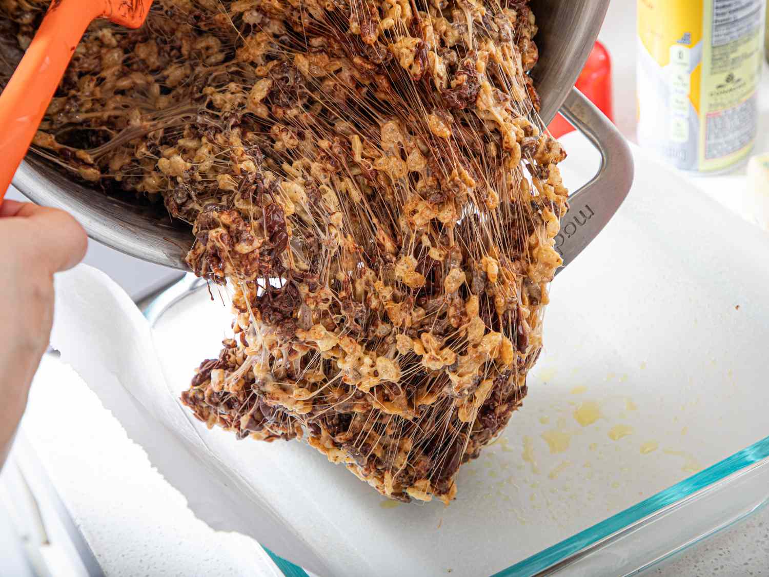 A mix of malted rice Krispies being poured into a dish from a pot using a utensil