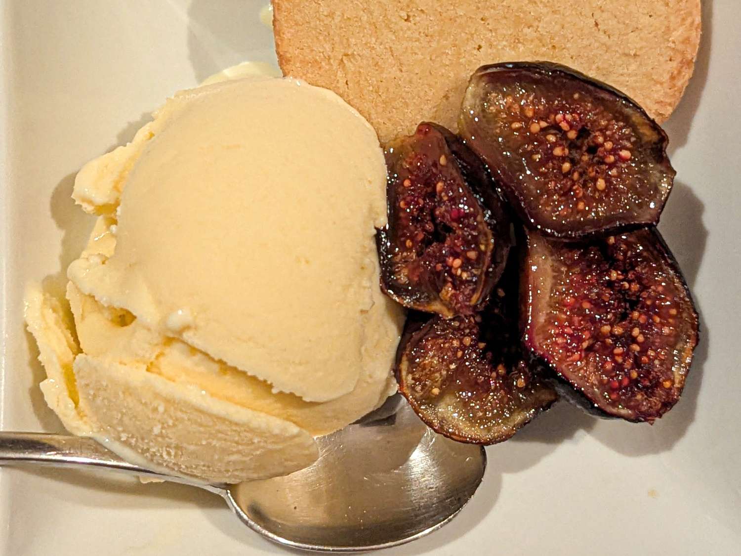 A serving of ice cream with figs and a slice of shortbread on a white plate